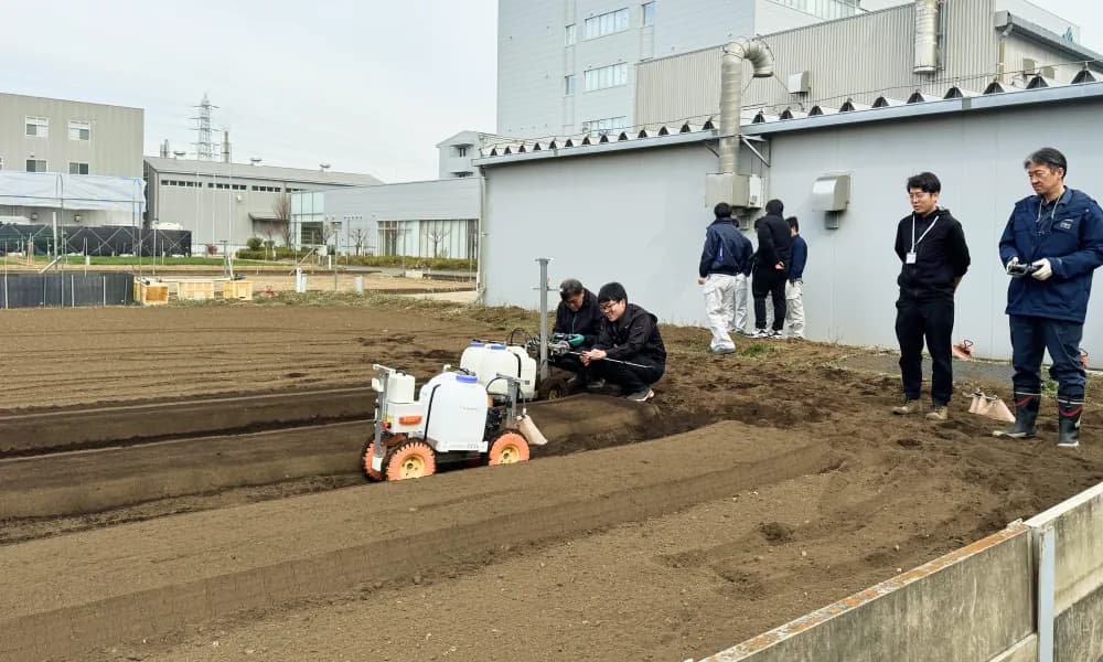ほ場で自動走行ロボットの実証実験を見学する人たち